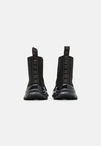Bottines en tricot noir avec un dessus texturé, une semelle lisse et brillante, et des languettes contrastées avec le logo à l'arrière.