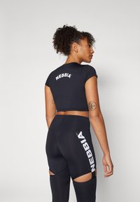 Juodas trumpas viršus ir leggingai su logotipu; prigludęs dizainas, trumpi rankovės, išpjovos ant leggingų, lygi tekstūra ir tampri medžiaga.