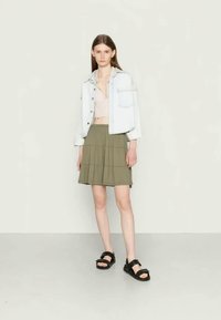 Jaqueta de ganga azul clara, top cropped rosa, saia em camadas verde-oliva e sandálias pretas com tiras. Exibição de um conjunto simples e casual.