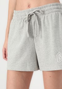 Lys grå bomullsshorts med elastisk midjebånd og snor. Har en liten hvit brodert bokstav "G" på nedre siden.