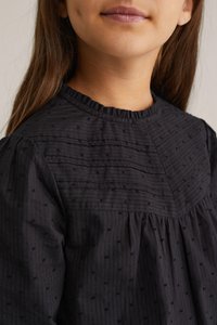 Svart klänning med högt, volangt halsringning, texturerad tyg med små prickar och vertikala ränder, långa puffärmar och rynkad byst.