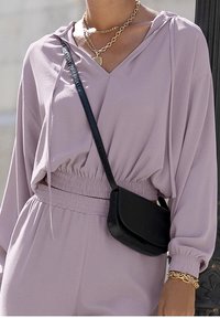 Lavendelfärgad oversized hoodie med V-ringning och elastisk midjeband, kombinerad med en svart texturerad axelväska och lager-på-lager guldkedjor.