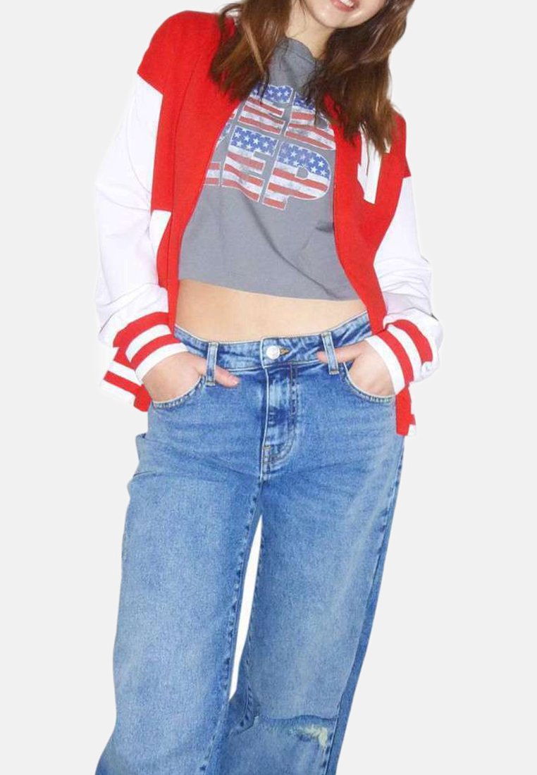 Une veste varsity rouge et blanche sur un t-shirt court gris avec un imprimé graphique. Un jean bleu clair taille haute avec une coupe décontractée.