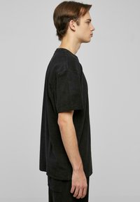 Černé oversized bavlněné tričko s kulatým výstřihem a krátkými rukávy, s měkkou texturou a rovně střiženým spodním lemem. Stylizováno s odpovídajícími kalhotami.