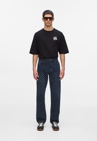 Zwarte korte mouwen t-shirt met grafische print, gecombineerd met blauwe wijde broek met patroon in houndstooth-ontwerp en zwarte sneakers.