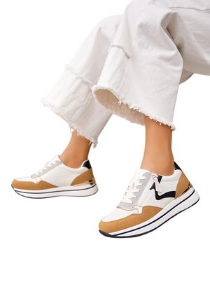 Baskets de sport blanches et beiges avec une tige texturée, des accents noirs contrastants et un détail métallique au niveau du talon.
