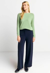 Hellgrüner, strukturierter Pullover mit rundem Hals, kombiniert mit weit geschnittenen, marineblauen Hosen und schwarzen Sportschuhen. Einfaches, lässiges Outfit.