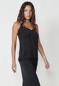 Črna satenasta camisole z čipkastim robom, V-izrezom in tankimi naramnicami. Ujemajoče se črne hlače širšega kroja. Gladka tekstura, minimalističen dizajn.