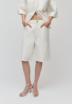 Shorts de mezclilla blanca con un corte relajado, que cuentan con bolsillos frontales y cierre de botón. El material tiene una textura suave y un diseño minimalista.