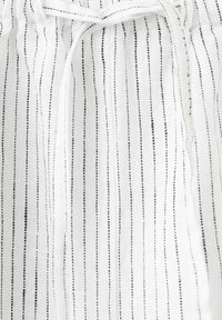 Biely textil s tenkými čiernymi vertikálnymi pruhmi a stiahnutým šnúrkovým zapínaním v hornej časti, ukazujúci textúrovaný, ľahký materiál.