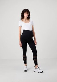 Leggings noirs avec des panneaux transparents rayés sur le bas des jambes, taille haute, assortis à un haut blanc à manches courtes et des chaussures de sport.