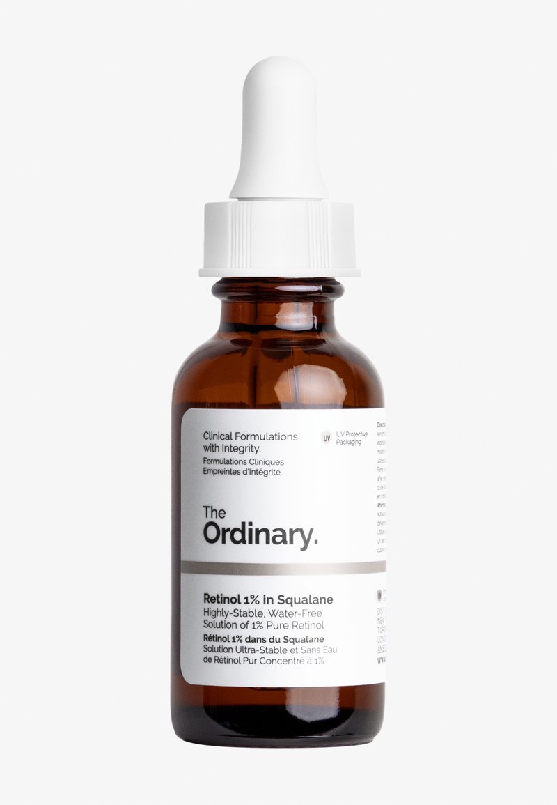 Amber glazen pipetfles met een witte dop. Bevat Retinol 1% in Squalane. Etiket met tekst in zwart en grijs op een witte achtergrond.