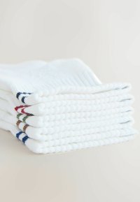 Pile de six chaussettes blanches pliées avec des rayures colorées aux poignets, posées sur une surface claire.