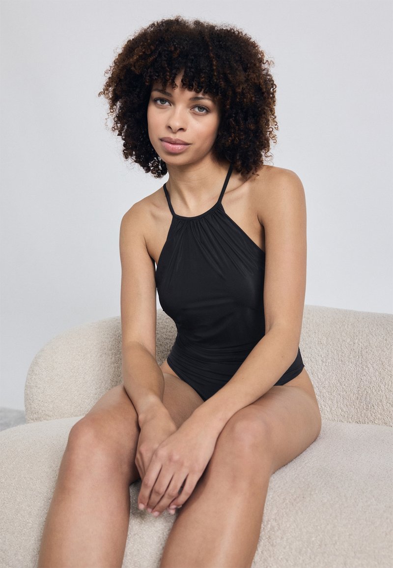 Crni kupaći kostim s halter izrezom, skupljenim materijalom, tankim trakama i glatkom teksturom. Dizajn sadrži prilagođenu siluetu i minimalne detalje.