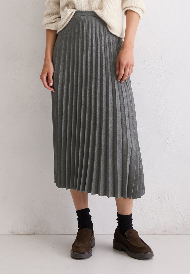 Grauer, gefalteter Rock aus weichem, strukturiertem Stoff, der bis zur Mitte des Waden reicht. Kombiniert mit dunklen Socken und braunen Slippern.