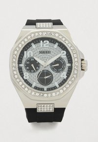 Ασημένιο ρολόι Guess με μαύρο καντράν, κρύσταλλο στην στεφάνη, τρεις υποκαντράν και μαύρο λουράκι από καουτσούκ με κρυστάλλινες λεπτομέρειες.