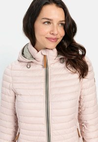 Lys pink kviltet jakke med aftagelig hætte, der har lynlås, snøre-detaljer og tan-farvede accenter på hætten og lommerne.
