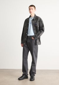 Mørk denimjakke over en lyseblå t-shirt, parret med mørke jeans og sorte sneakers. Inkluderer en halskæde og minimalistiske designelementer.
