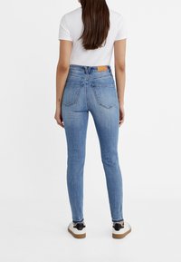 Džíny z modrého denimu s vysokým pasem a slim fit. Mají dvě zadní kapsy a koženou nášivku na pasu. Nosí se s bílým tričkem a teniskami.