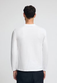 T-shirt bianco a maniche lunghe in cotone, con collo rotondo e vestibilità rilassata, orlo dritto e dettagli di cucitura minimi.