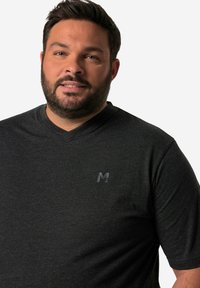 Camiseta de corte corto, de color gris oscuro y con cuello en V, hecha de una tela suave, con un sutil logo negro en el pecho. Diseño simple y moderno.