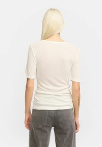 Valkoinen ribattu t-paita lyhyillä hihoilla, jossa on aaltoileva helma ja pilkullinen pinta. Yhdistettynä harmaisiin korkeavyötäröisiin farkkoihin.