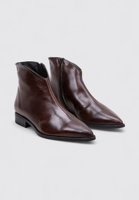 Bottes en cuir marron jusqu'à la cheville avec un bout pointu, un design épuré et une fermeture éclair sur le côté. Elles disposent d'un petit talon carré et d'une texture lisse.