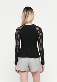 Haut peplum noir avec de longues manches en dentelle, présentant un buste ajusté et un design texturé. Associé à un short gris clair.