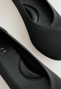 Schwarze Slip-On-Schuhe mit einer strukturierten Strickoberfläche und einer glatten schwarzen Innensohle mit kleinen punktierten Prägungen. Einfaches, rundes Zehendesign.