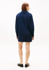 Μακρυμάνικο φόρεμα σε ναυτικό μπλε με γιακά, κατασκευασμένο από απαλό ύφασμα, με άνετη εφαρμογή που φτάνει μέχρι το μέσο του μηρού, συνδυασμένο με μαύρα παπούτσια.