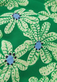 Bloemstof met grote groene bloemen met lichtgroene bloemblaadjes, blauwe centra en zwarte accenten, tegen een levendige groene achtergrond.