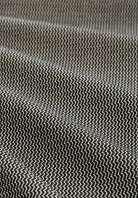 Textiel met een zigzagpatroon in zwart en wit, met een gestructureerde oppervlakte en zichtbare plooien en variërende tinten.