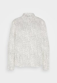 Chemise blanche à manches longues avec motif de petits pois noirs irréguliers et col classique, posée à plat sur un fond uni.