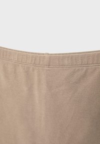 Tissu beige avec ceinture élastique visible et détail de couture, montrant la texture et l'élasticité en gros plan.