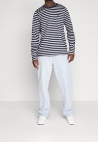  långärmad skjorta i marinblått och beige ränder med rund hals, kombinerad med ljusblå baggy jeans och vita sneakers.