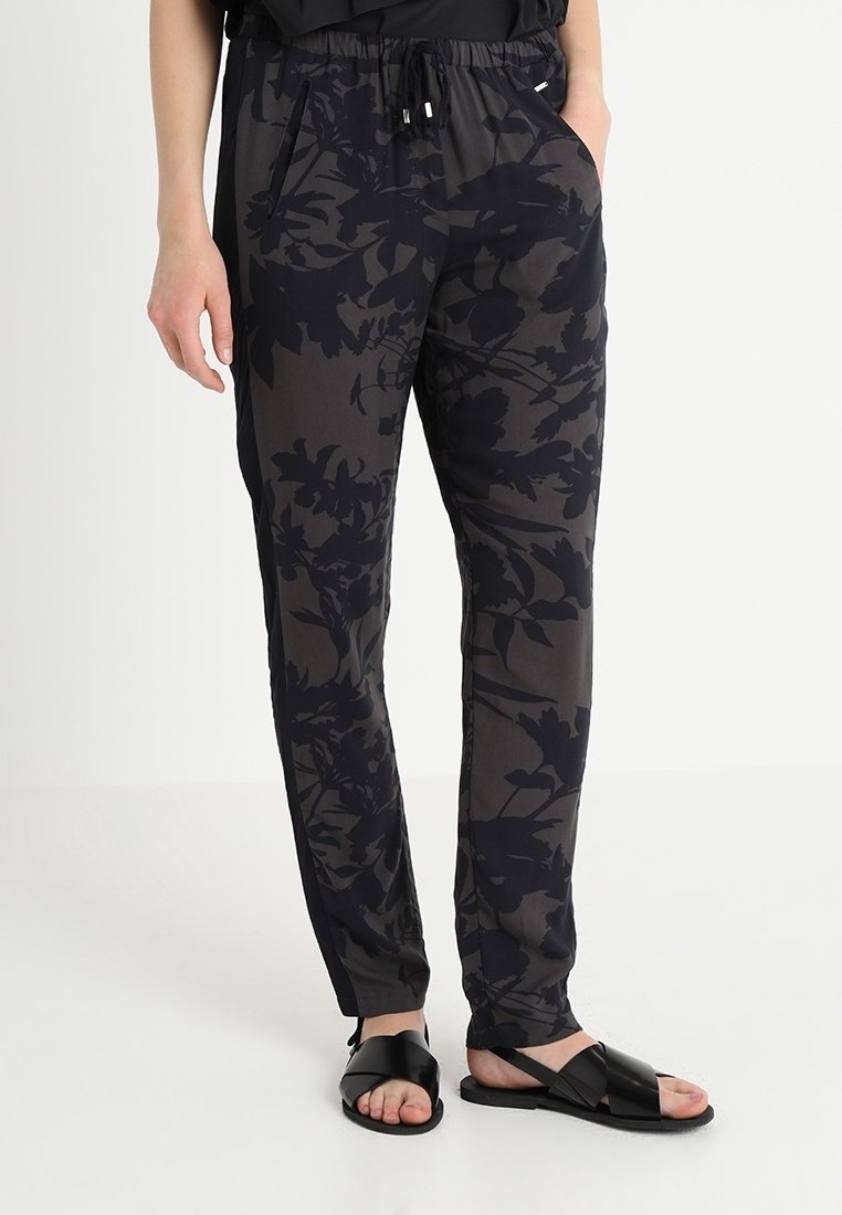 Pantalons noirs et gris à motif avec une taille élastique, des poches latérales et une coupe décontractée, associés à des sandales noires.