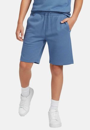 Blauwe korte broek van een katoenmengsel met een elastische tailleband en een trekkoord. Voorzien van zijzakken en een knielange snit. Draagt wit sneakers.