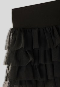 Gonna nera con una vita aderente e liscia, adornata da strati di volant in tulle nero. Il livello superiore presenta una finitura testurizzata che contrasta con i livelli inferiori trasparenti.