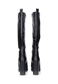 Botas de piel negras por encima de la rodilla con una textura suave, costuras prominentes y tacones gruesos, que cuentan con cremalleras traseras para el cierre.