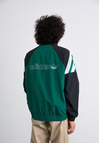 Green and black jacket with white accents, featuring an elasticated waist and cuff, and the "adidas" logo on the back.
