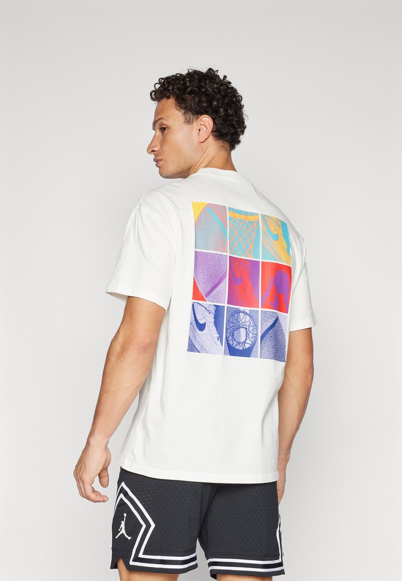 White cotton t-shirt featuring a multicolored graphic design on the back with various patterns. Short sleeves and a crew neckline.