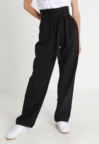 Pantalons noirs taille haute avec une jambe large, dotés d'une ceinture nouée à la taille. Le tissu semble lisse avec une coupe structurée.