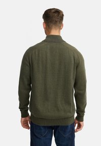 Mørkegrøn sweater med ribbet krave og manchetter. Har et struktureret strikket mønster, lange ærmer og en tætsiddende talje. Casual design.