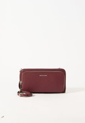 Bordeauxfarbige Michael Kors Leder-Armbandtache mit vorderer Reißverschlusstasche und abnehmbarem Riemen auf weißem Hintergrund.