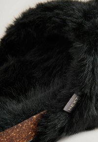 Sort faux fur sutsko med en struktureret overflade. Har en korksål og et mærke med "NEXT" syet på indersiden. Blødt og hyggeligt design.