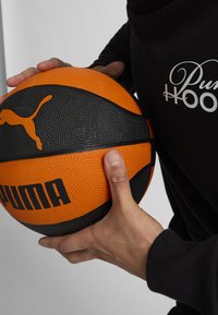 Pallone da basket con un design diviso tra arancione e nero con superficie testurizzata. Logo nero e la scritta "PUMA" in evidenza.