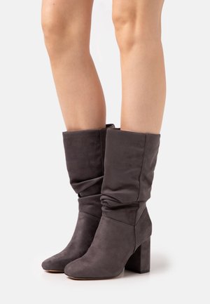 Bottines grises décontractées en suède doux, avec un bout pointu et un talon épais, présentant des détails de couture subtils.