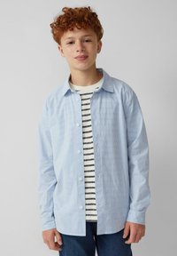 Lichtblauw gestreept shirt met een knoopsluiting aan de voorkant, lange mouwen en een losse pasvorm, gelaagd over een zwart-wit gestreept T-shirt.