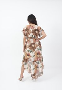 Il vestito maxi floreale presenta un tessuto leggero e trasparente, con ampi motivi floreali marroni e rosa, maniche corte a sbuffo e una vita aderente.