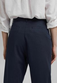 Pantalon bleu marine à la texture lisse, doté de poches arrière et d'une coupe slim, associé à une chemise blanche ample.